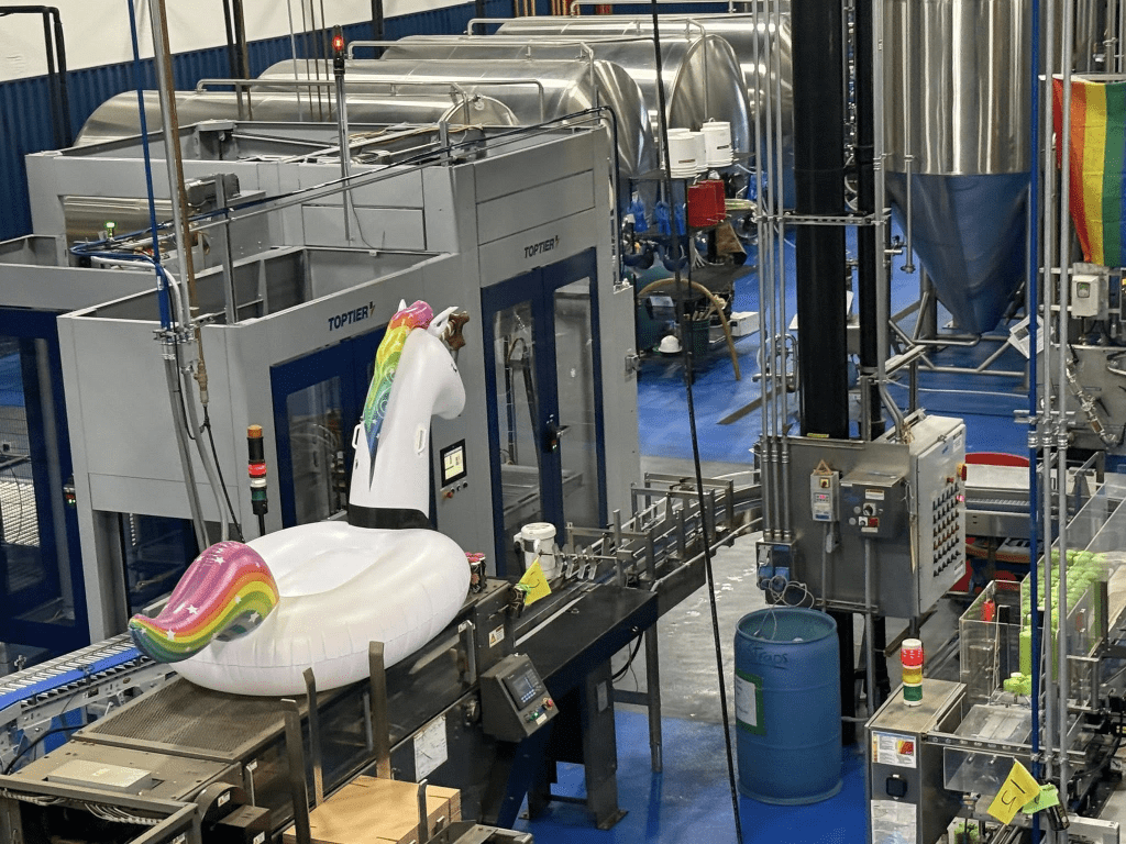 An industrial setting featuring machinery and equipment, with an inflatable unicorn pool float placed on a conveyor belt.