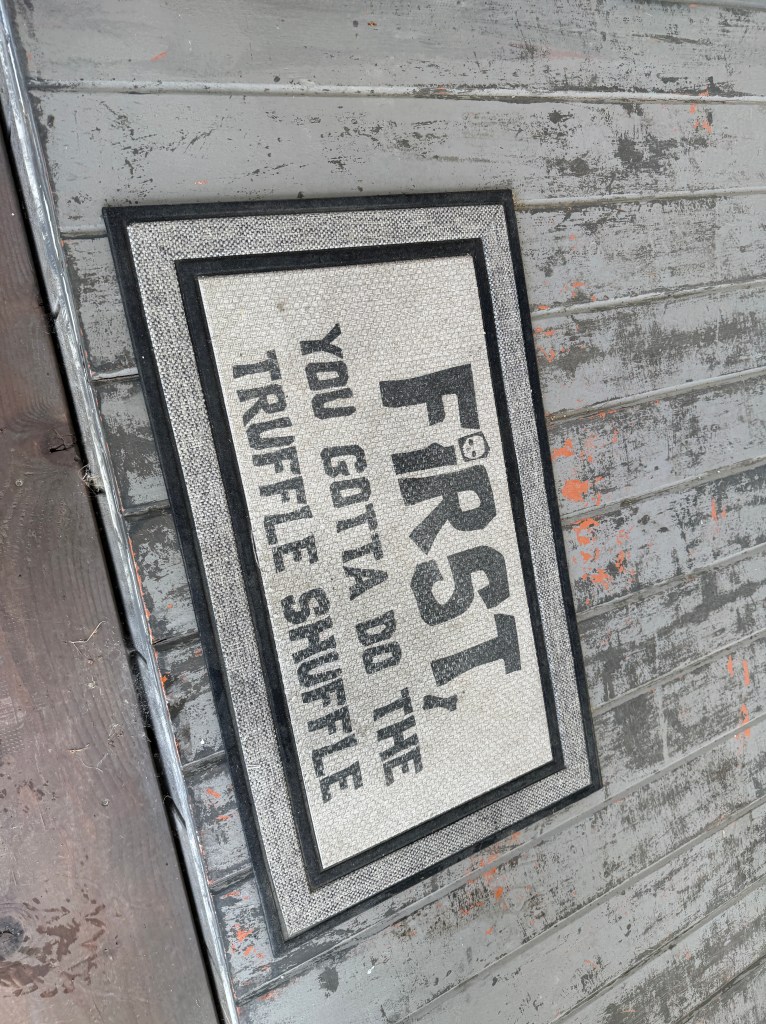 A doormat featuring the text, 'FIRST, YOU GOTTA DO THE TRUFFLE SHUFFLE,' set against a textured background.