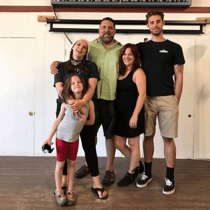 A group of five people posing for a photo in a casual indoor setting, including two adults in the back, two adults in the front, and a young girl in the center.