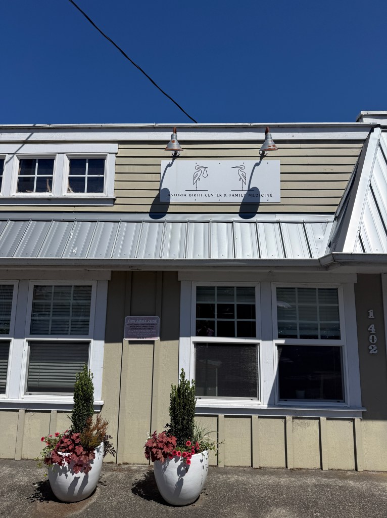 Exterior view of the Astoria Birth Center and Family Medicine building, featuring a sign with the center's name and decorative planters on either side.