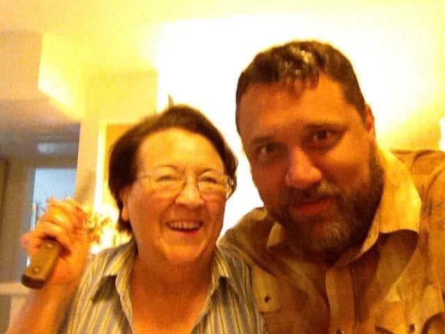 A smiling older woman and a man take a selfie together in a bright, homey setting.