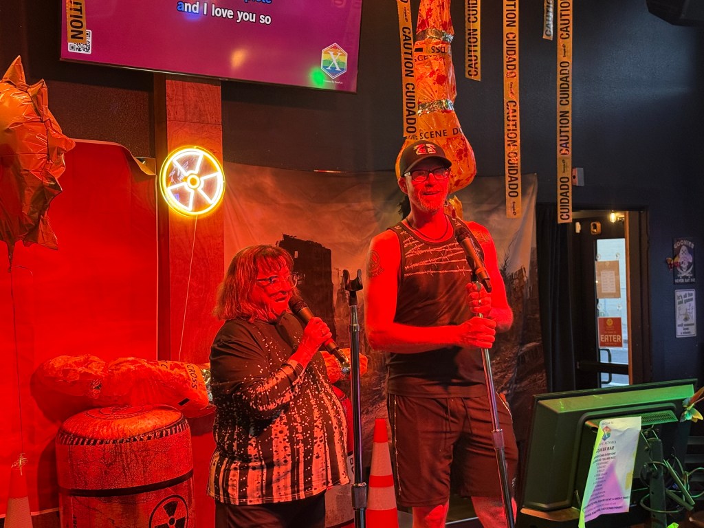 Two individuals perform karaoke in a lively venue, surrounded by colorful decorations and themed lighting.